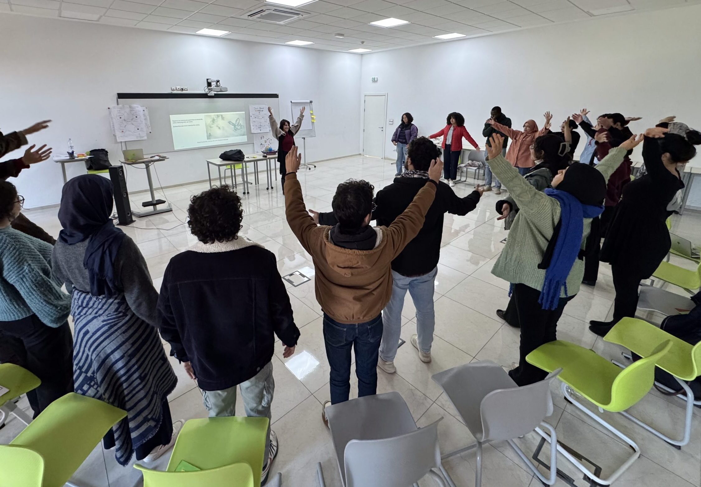 University students engaging in a collective grounding exercise during a TEP workshop, using embodied movement to build trust, emotional regulation, and group cohesion prior to dialogical work on sensitive issues.